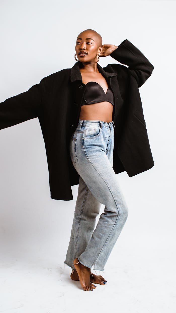 A confident young black woman posing in a studio with a modern look in denim and a black jacket.
